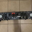 Zadní strana černého rackového zesilovače s dvěma chladicími ventilátory. Jsou zde viditelné nápisy INPUT AC, FUSE T5AL230V, OUT B, OUT A, IN B, IN A…
