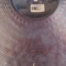 Detailní záběr na kovový činel s kovaným povrchem. V dolní části je viditelné logo Zildjian. Na činelym je nalepená štítková nálepka s nápisy Zildjia…