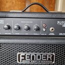 Černý basový kombo zesilovač s logem FENDER BASS AMPLIFICATION na přední mřížce a v levém horním rohu. Na ovládacím panelu je nápis RUMBLE 15 a 15W B…