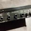 Černý kovový panel s řadou konektorů a nápisy. Jsou zde viditelné popisky Footswitch, Right Out, Left Out, Headphone a Line Out, dále přepínač +4 dB…