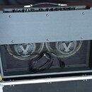 Zadní strana kytarového komba v šedém potahu s černou síťovkou. Jsou vidět dva reproduktory s logem V a nápisem Celestion. K přístroji je připojen na…