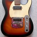 Elektrická kytara s tělem v provedení sunburst a krémovým pickguardem. Nástroj má dva snímače, jeden v pozici hradla a druhý u mostu s kovovým krytem…