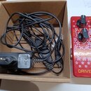V hnědé kartonové krabici je smotaný černý napájecí kabel s adaptérem. Na adaptéru je viditelné logo BOSS a nápisy: "INPUT: 100-240V AC 50/60Hz", "OU…