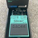 Kytarový efekt Boss SL-2 Slicer v tyrkysovém provedení, umístěný ve své originální černé krabici. Na pedálu jsou viditelné tři ovládací knoflíky a ná…