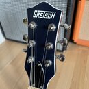 Fotografie zachycuje hlavu elektrické kytary v tmavě modré barvě s bílým lemováním. V horní části je bílý nápis GRETSCH. Na hlavě jsou instalovány še…