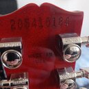 Zadní strana hlavy červené kytary s viditelným sériovým číslem 205410184 a nápisem MADE IN USA. Na hlave jsou instalovány chromované ladicí mechanism…