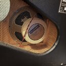 Detail reproduktoru v černém boxu s kovovou mřížkou. Na středovém krytu reproduktoru je vidět nápis CELESTION. V pravém horním rohu je štítek s texte…