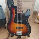 Elektrická basová kytara s korpusem v barevném přechodu od černé přes červenou k žluté. Nástroj má černý pickguard, hnedý hmatník a čtyři struny. Na…