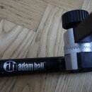 Detail černé kovové části stojanu s viditelným logem a nápisem "adam hall stands". Součástí je stříbrný kovový spoj s ozubeným mechanismem a černý pl…