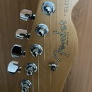 Fotografie zachycuje hlavu elektrické kytary z přírodního světlého dřeva s chromovanými ladičkami. Na dřevě je vidět logo Fender, nápis MADE IN U.S.A…