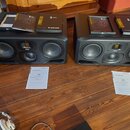 Dva černé studiové monitory značky ADAM AUDIO z řady S SERIES. Na horní straně obou reproduktorů leží manuály a dokumentace s nápisy S SERIES a ADAM…