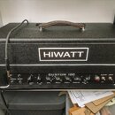Černý kytarový zesilovač s koženou rukojetí a bílým lemováním. Na předním panelu je bílé logo HIWATT a nápis CUSTOM 100. Ovládací panel obsahuje přep…