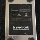 Spodní strana stříbrného efektového pedálu s černým štítkem. Na štítku je uveden nápis tc electronic a DESIGNED AND ENGINEERED IN DENMARK, dále MADE…