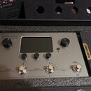 Stříbrný efektový procesor s nápisem AMPERO a podtitulem Amp Modeler & Effects Processor. Zařízení má centrální displej, dva otočné ovladače s popisk…