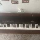Černý digitální klavír umístěný na hnědém dřevěném stole. Na pravé straně je bílý nápis YAMAHA a vedle něj modelové označení pf15. Nástroj má standar…