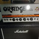 Kytarový zesilovač značky ORANGE s nápisem DUAL TERROR umístěný na kytarovém kombu značky Marshall. Zesilovač má bílý přední panel s ovládacími prvky…