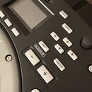 Detailní pohled na ovládací panel černého elektronického nástroje s displejem. Jsou vidět tlačítka s nápisy D-BEAM, MENU, EXIT, ALL SOUND OFF, ENTER,…