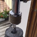 Detail horní části chromovaného stojanu s úpnutím. Na kovovém mechanismu je viditelný šroub s knoflíkem a pod ním hnědý gumový nebo plstěný kroužek.…