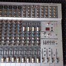 Stříbrný mixážní pult s nápisem MM1805X PHONIC. Zařízení obsahuje více vstupních kanálů s potenciometry, posuvníky a řadu konektorů v horní části. V…
