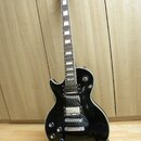 Černá elektrická kytara s tvarem typu Les Paul, osazená dvěma humbuckery a čtyřmi ovládacími knoflíky. Na hlavě nástroje je bílý nápis BACH a logo ve…