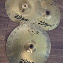 Tři mosazné činely s viditelným broušením povrchu. Každý z nich má nápisy Zildjian a PLANET Z. Na spodním činely je dále čitelný nápis CRASH 16" 40 c…