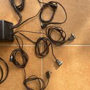 Fotografie zobrazuje černý napájecí adaptér, ze kterého vychází několik černých kabelů zakončených válcovými konektory. Kabely jsou rozprostřeny na h…