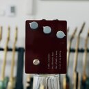 Tmavě červený efekt pedál s třemi světle šedými otočnými knoflíky a jedním kovovým spínacím tlačítkem. Na spodní části je bílý text: „Kindly remember…