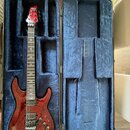 Elektrická kytara s červeným lakovaným tělem z dřeva s viditnou strukturou zrn a černým hardwarem. Na hlavě hmatníku je bílé logo „SCHECTER“. Nástroj…