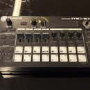 Černá groovebox s bílými popisky a tlačítky. Na horní hraně je nápis Roland vlevo a GROOVEBOX MC-101 vpravo. Zařízení obsahuje několik ovládacích kno…