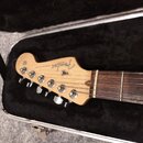 Detail hlavy a hmatníku elektrické kytary v otevřeném kufru s černým polstrováním. Na hlavě je vidět logo Fender, nápis STRATOCASTER a text MADE IN U…