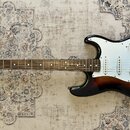 Elektrická kytara s trupem v černo-hnědém sunburst provedení a bílým pickguardem. Na hlavě hmatníku je nápis SKYLARK. Nástroj má tři snímače typu sin…