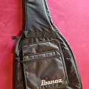 Černý poloměký pouzdro (gig bag) na kytaru. Na přední kapse je bílý nápis Ibanez. Povrch materiálu vykazuje mírné pomačkání a známky používání.