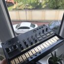 Černý elektronický sampler s názvem vokabeat a logem KORG. Zařízení obsahuje řadu ovládacích knofíků, tlačítek a spodní sekci s bílými políčky popsan…