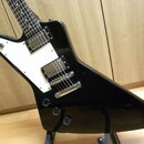 Černá elektrická kytara s bílým pickguardem a dvěma humbuckery. Tělo má atypický, ostře zakončený tvar. Na spodní části těla jsou tři ovládací knofík…