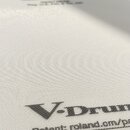 Bílá bubnová plocha s jemnou mřížkovou strukturou. V horní části je logo Roland a pod ním nečitelný text. Ve spodní části je velký nápis V-Drums a po…