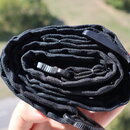 Černý textilní popruh, pravděpodobně kytarový řemen, srolovaný do spirály. Na popruhu jsou vidět černé plastové přezky. Povrch materiálu je tkaný a v…
