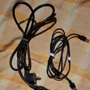 Na fotografii jsou dva černé napájecí kabely. Jeden je standardní síťový kabel s kolmou vidlicou a konektorem typu C13. Druhý je kratší kabel s konek…