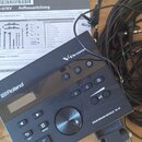 Na fotografii je černý elektronický bicí modul s nápisy Roland, V-Drums a DRUM SOUND MODULE TD-07. Vedle modulu jsou svázané černé kabely a černý nap…