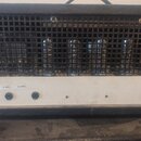 Černý kytarový zesilovač s kovovou mřížkou, za kterou jsou vidět elektronky. Na bílém spodním panelu jsou nápisy 4 OHM, 8 OHM a 16 OHM u přepínačů a…
