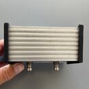 Stříbrný kovový box s žebrovaným povrchem a černými plastovými krajními částmi. Na spodní straně jsou umístěny dva kovové konektory. Povrch vykazuje…