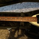 Elektrická kytara s bílým tělem a hnědým hmatníkem, uložená v černém pouzdře. Na těle je vidět černý pickguard a struny. Nástroj nemá žádné viditelné…