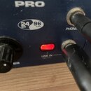 Detailní záběr na modré kovové zařízení s nápisem PRO a označením 24 BIT 96 kHz. Na přední straně je černý ovrtací knoflík, červen게 svítící kontrolka…