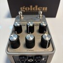 Stříbrný efektový pedál s šesti černými otočnými knoflíky a třemi přepínači. Na horní straně je nápis golden REVERBERATOR a pod knoflíky jsou popisky…