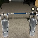 Kosový dvojpedál na bubny v kombinaci stříbrného kovu a modrého anodovaného povrchu. Na obou pedálech je viditelné logo a nápis YAMAHA. Součástí je m…