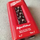 Červený DI box s rýhovaným povrchem. Na horní části je nápis RED BOX a v dolní části logo Hughes & Kettner s varovným textem Never use tube amps with…