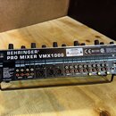 Černý mixážní pult s nápisem BEHRINGER® PRO MIXER VMX1000. Na zadní straně jsou vidět různé vstupy a výstupy, včetně konektorů pro napájení, efektů,…