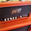 Kytarový kombozesilovač v oranžovém vinylu s černou přední síťovkou, na které je umístěno logo HOT. Ovládací panel obsahuje bílé a červené knoflíky s…