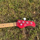 Fotografie zachycuje hlavu a část hmatníku basové kytary v červené barvě. Na hlavě je bílý nápis s logem a textem GUITARS & BASSES Jabda. Nástroj má…