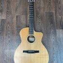 Akustická kytara s vyřezem (cutaway) a přírodní barvou dřeva. Na hlavě je viditelné logo "Taylor". Nástroj vykazuje čistý povrch bez viditelných pošk…