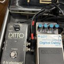 Dvě efektové pedály v černém kufru, propojené kabely. Vlevo je šedý pedál s nápisy „DITTO“, „STEREO LOOPER“, „true bypass“ a logem „tc electronic“. V…